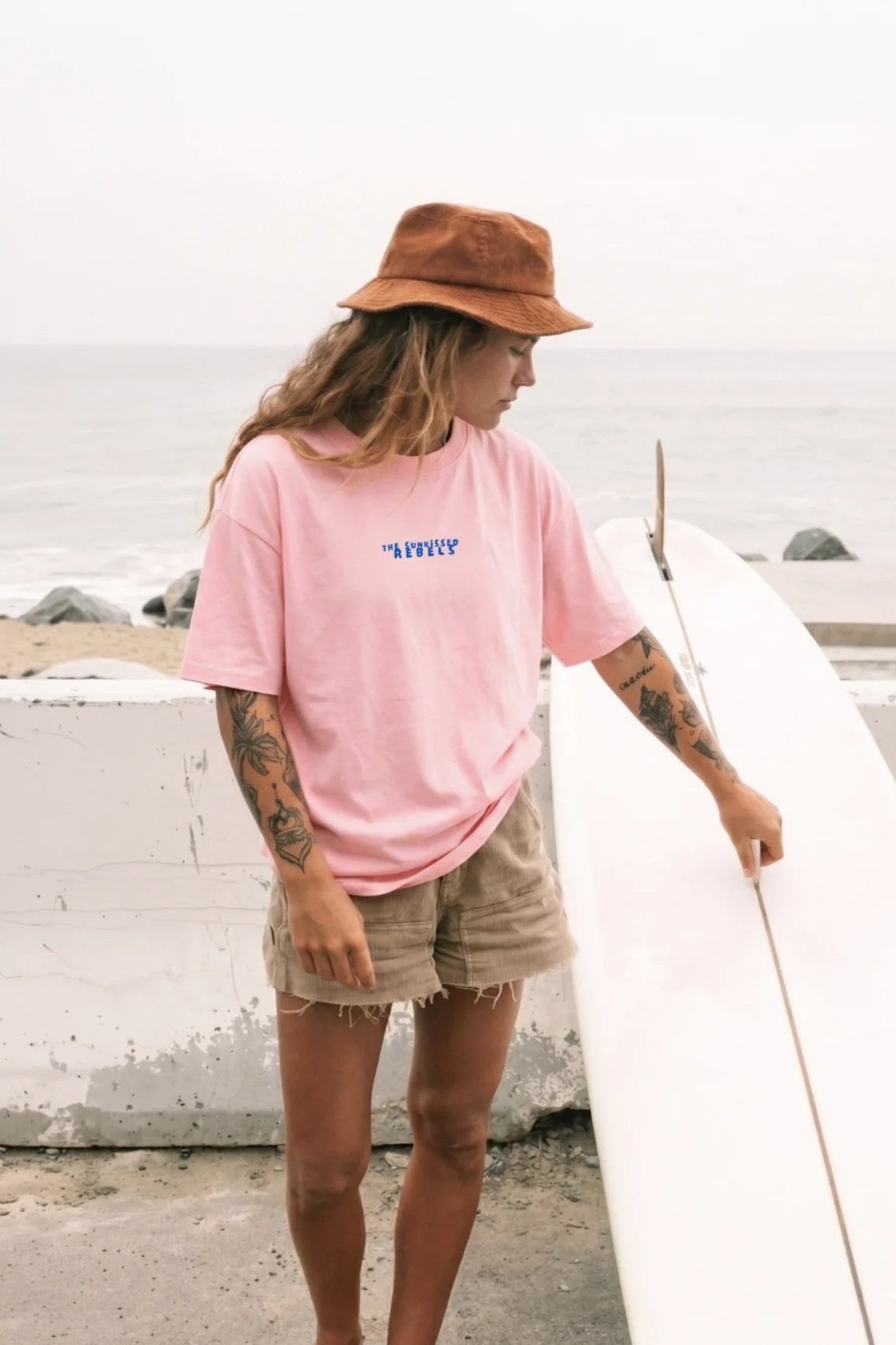 Frau am Strand im rosa No Bullshit Whale Boxy Oversized T-Shirt von The Sunkissed Rebels mit blauem Logo-Print auf der Brust