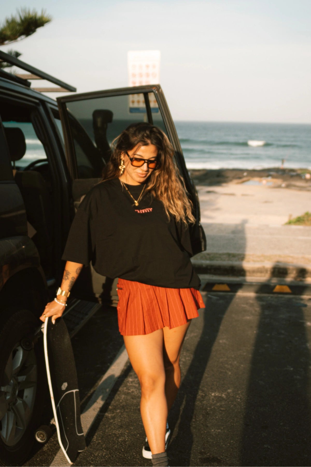 Skaterin mit dem No Bullshit Whale T-Shirt in Schwarz steht am Auto mit Blick mit skateboard min der hand.