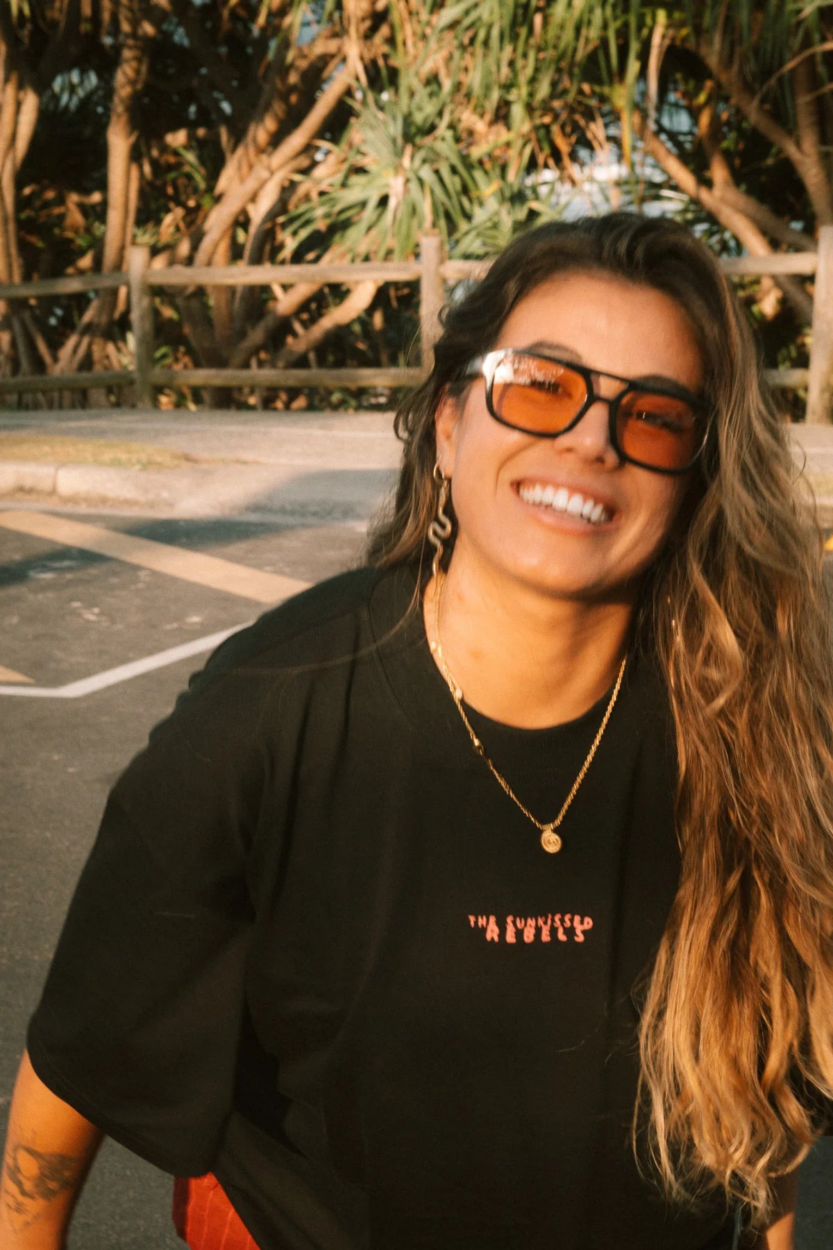 Frau trägt das No Bullshit Whale T-Shirt Black – Sommerlook mit Skateboard an der Küste.