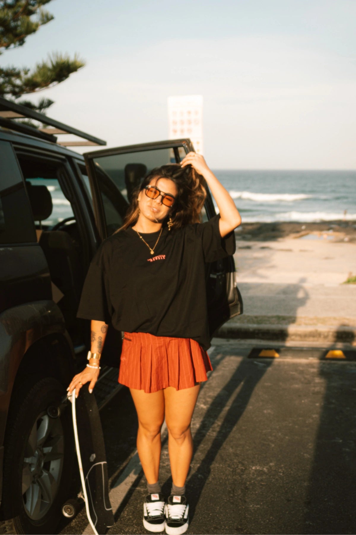 Frau trägt das No Bullshit Whale T-Shirt Black – Sommerlook mit Skateboard an der Küste.