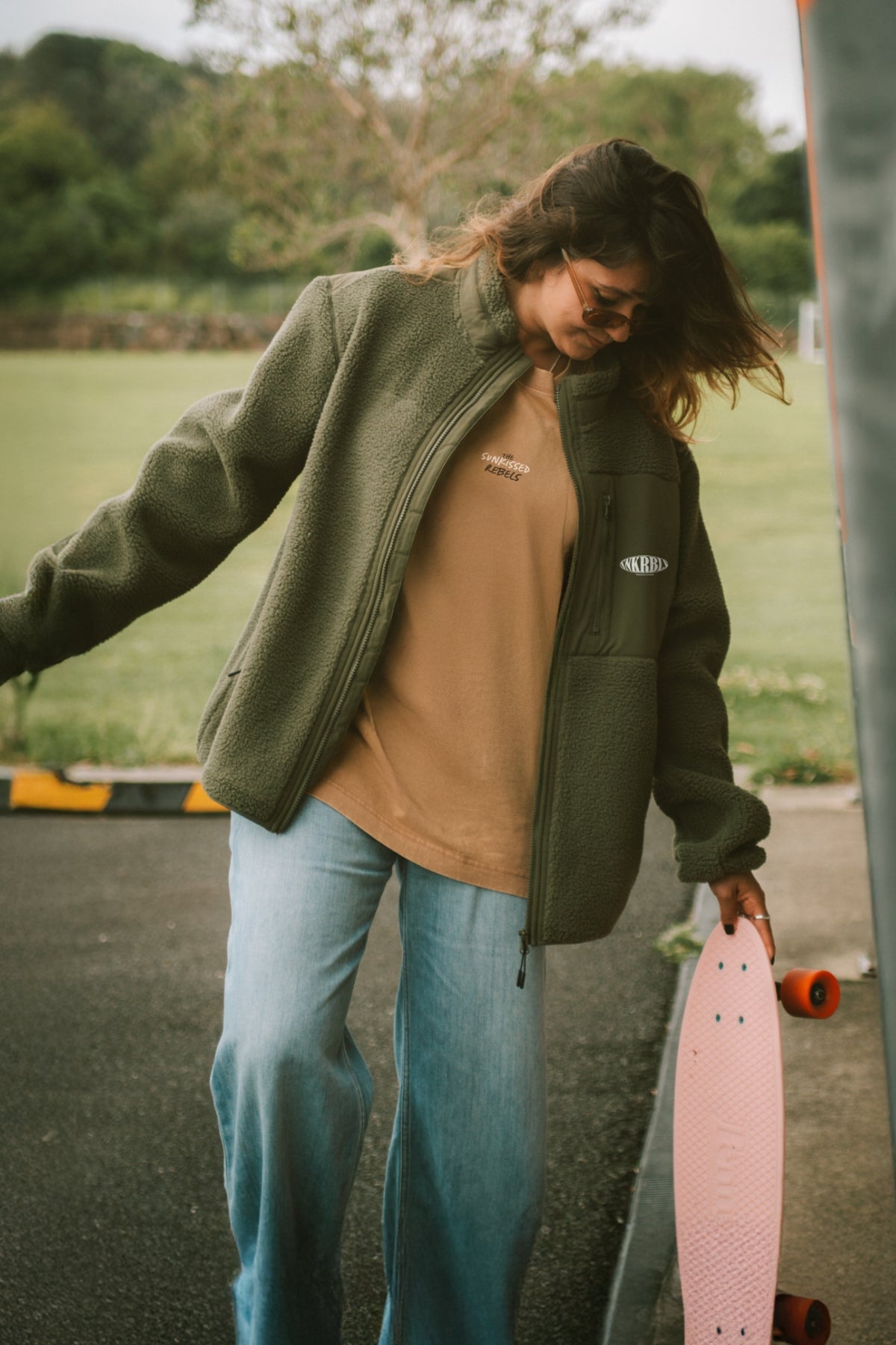 frau hält skateboard in der hand und trägt grüne fleece jacke