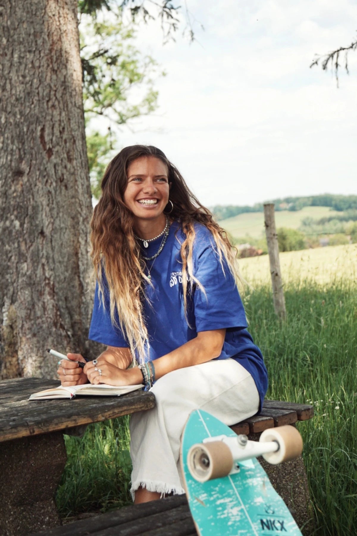  Frau sitzt an einem Picknicktisch im Grünen, trägt lockeres Statement-Shirt mit „Everyday is a Good Day“
