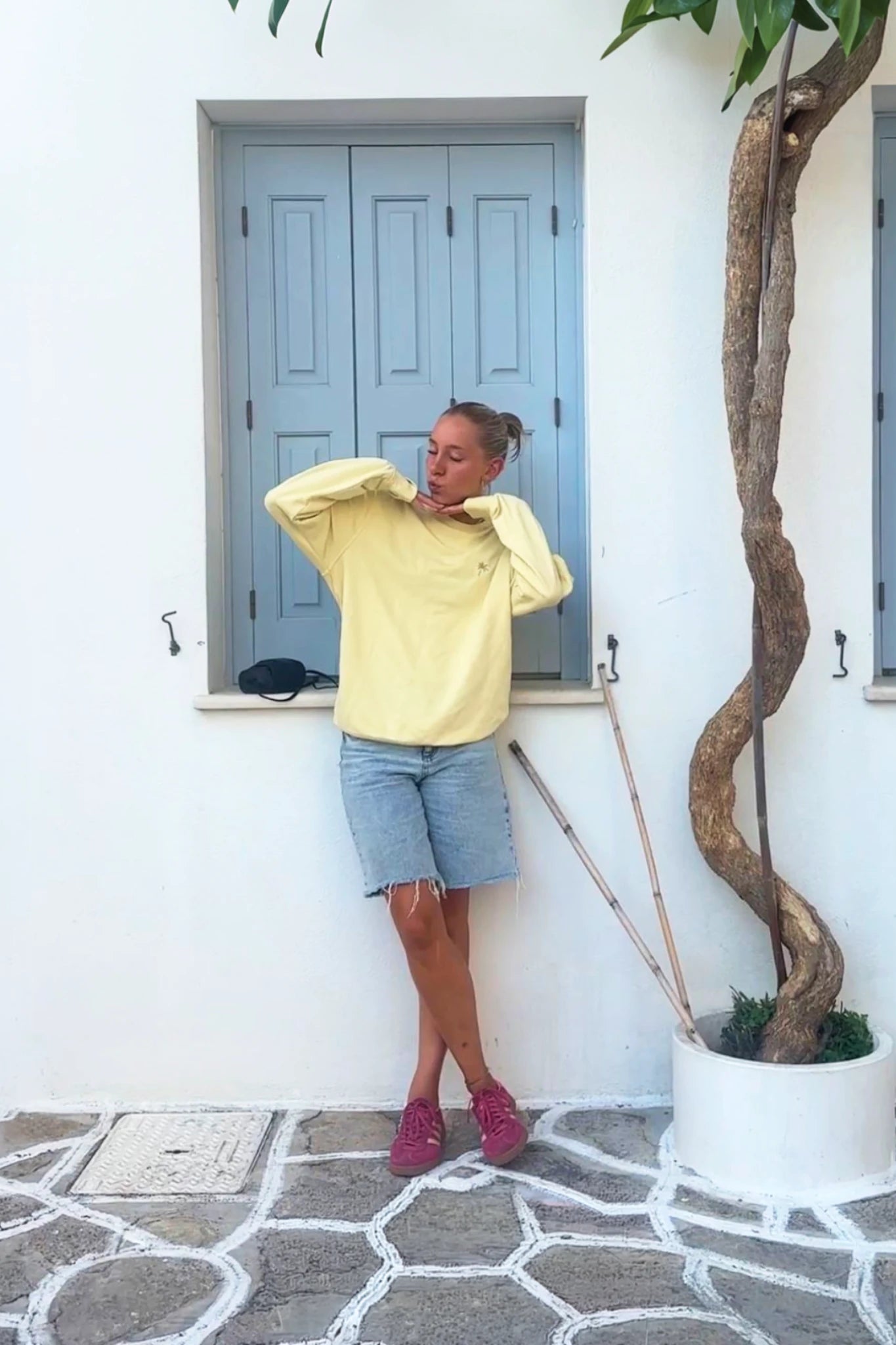 Frau lehnt entspannt vor Fenster und trägt gelben Palm Tree Sweater Butter – casual Streetwear Look mit Sommer Stil