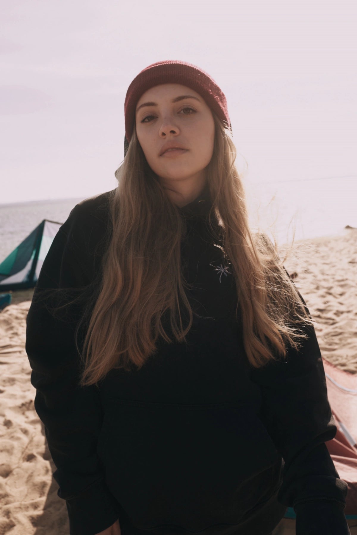 Model von The Sunkissed Rebels trägt den Palm Tree Vintage Hoodie Black am Strand mit Meer im Hintergrund