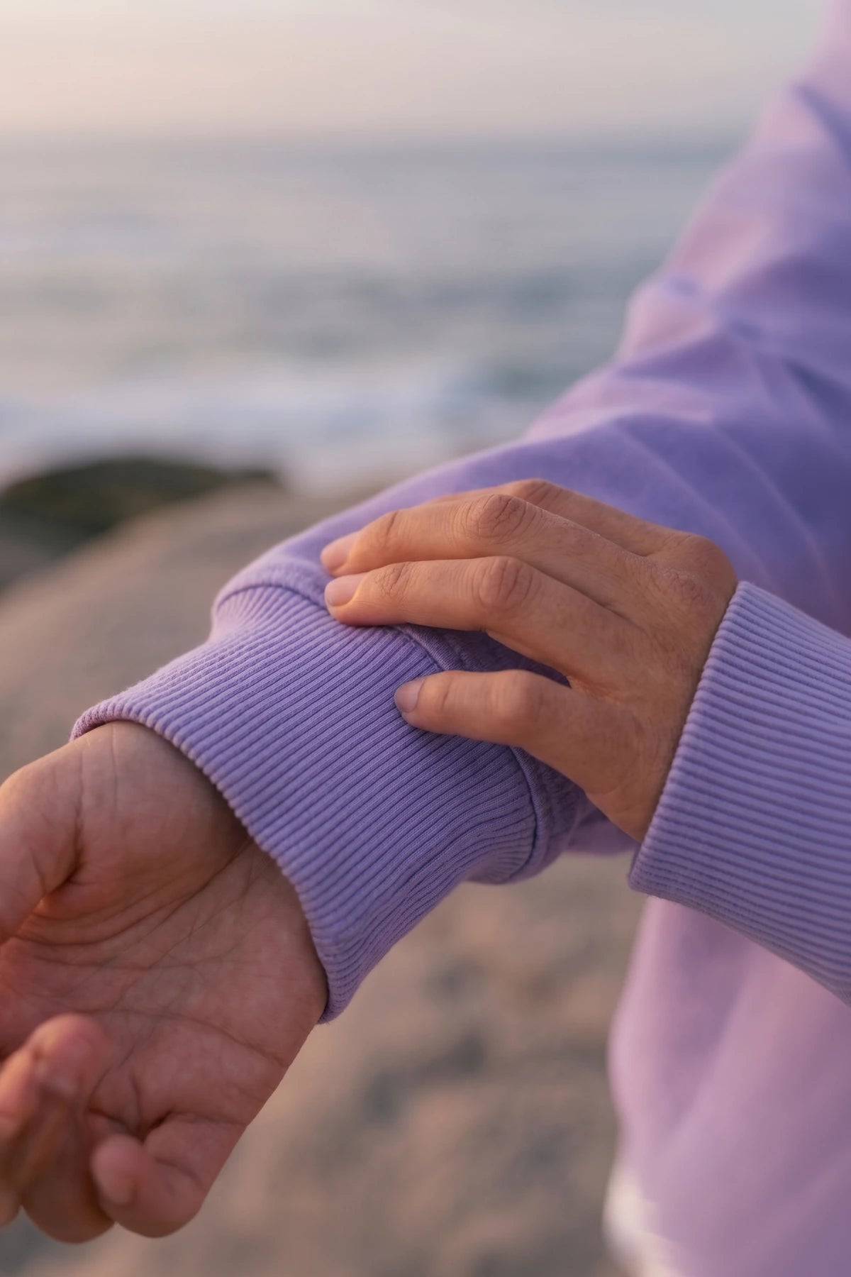 Detailaufnahme des Pink Palm Oversized Vintage Sweater Violet mit weichem Stoff und oversized Ärmel am Strand bei Sonnenuntergang