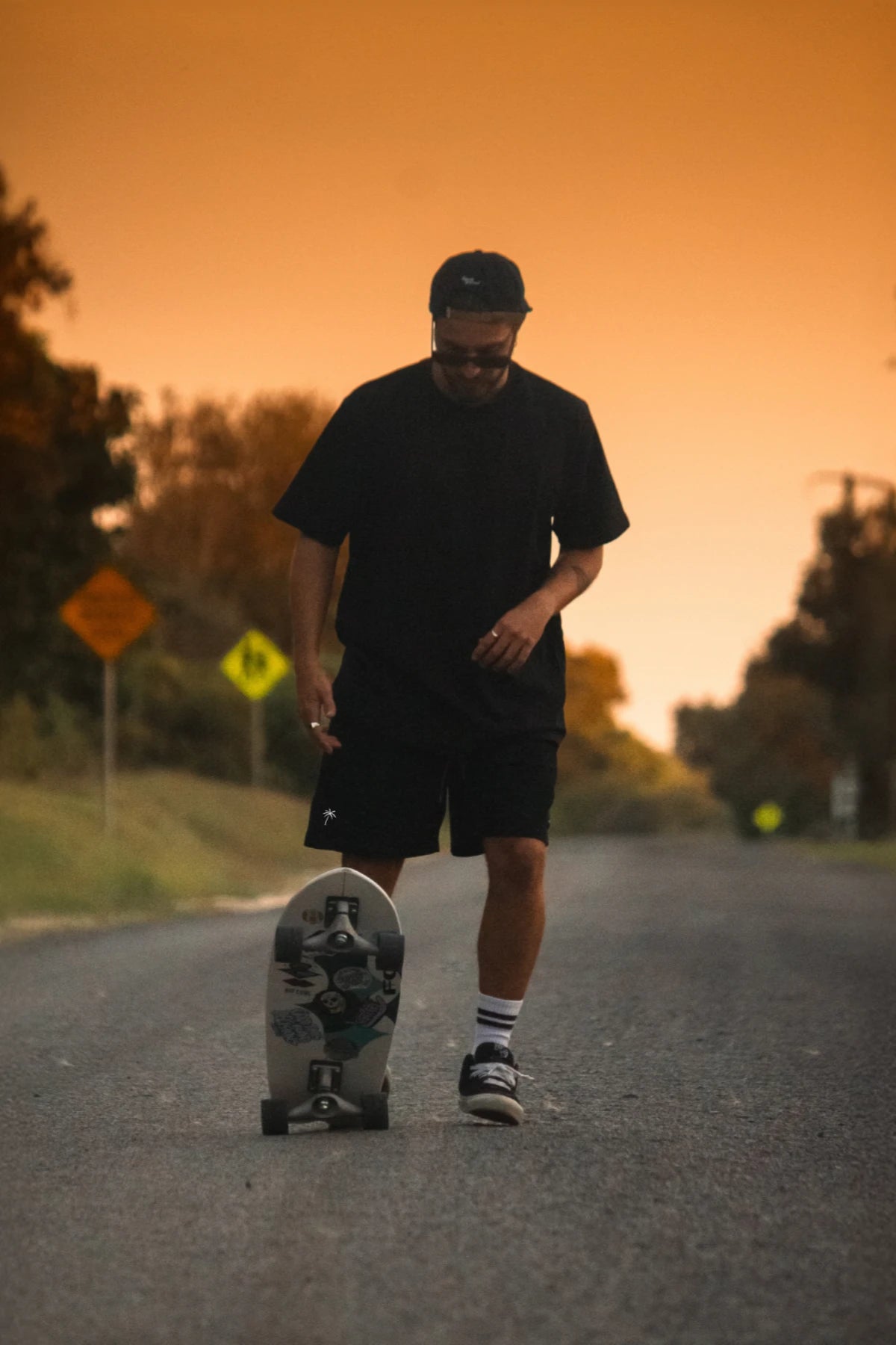 Mann mit schwarzem oversized T-Shirt und Sonnenbrille in goldener Abendsonne auf Landstarße in Australien
