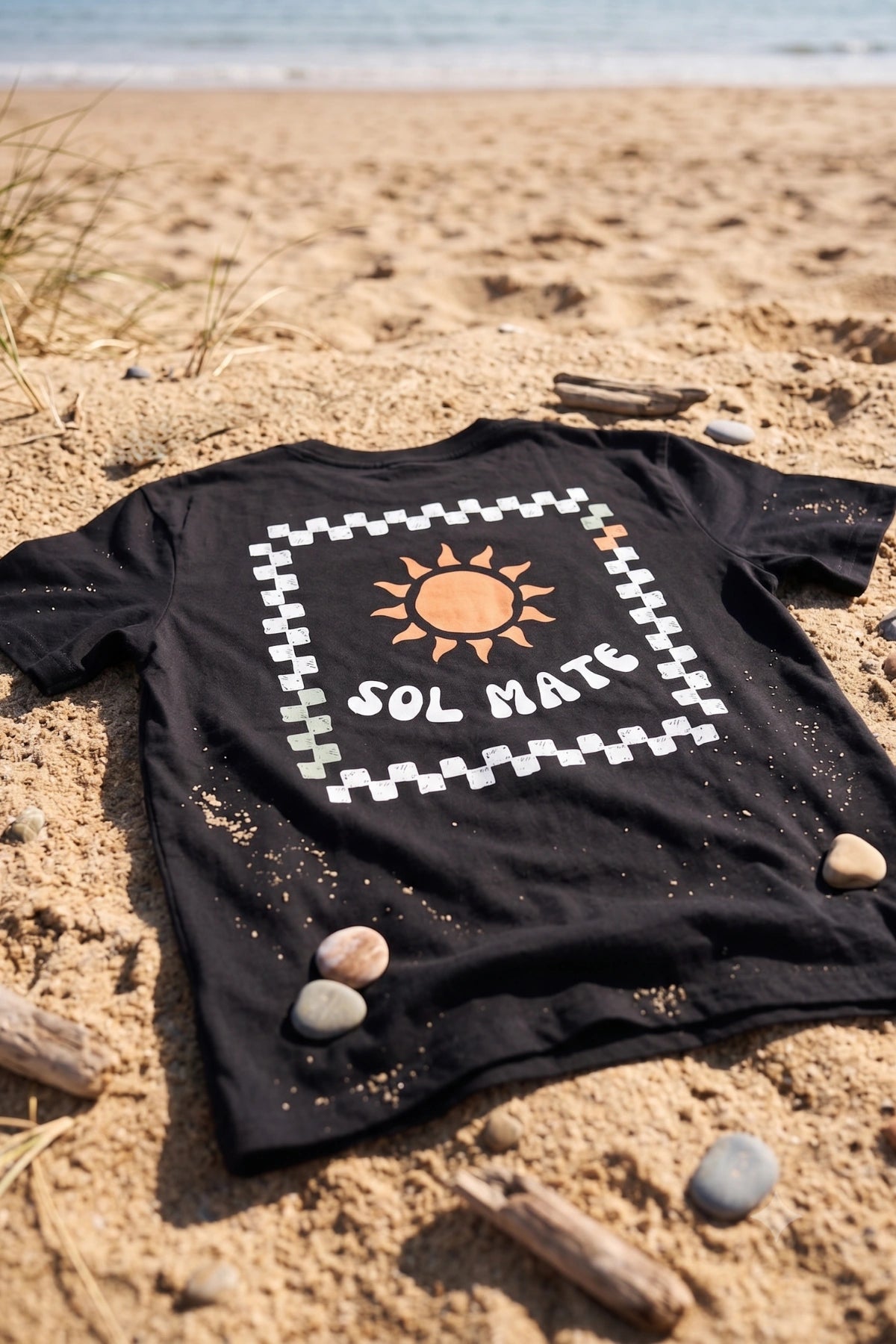 Schwarzes Sol Mate Oversized T-Shirt von The Sunkissed Rebels im Flatlay auf Sand am Strand