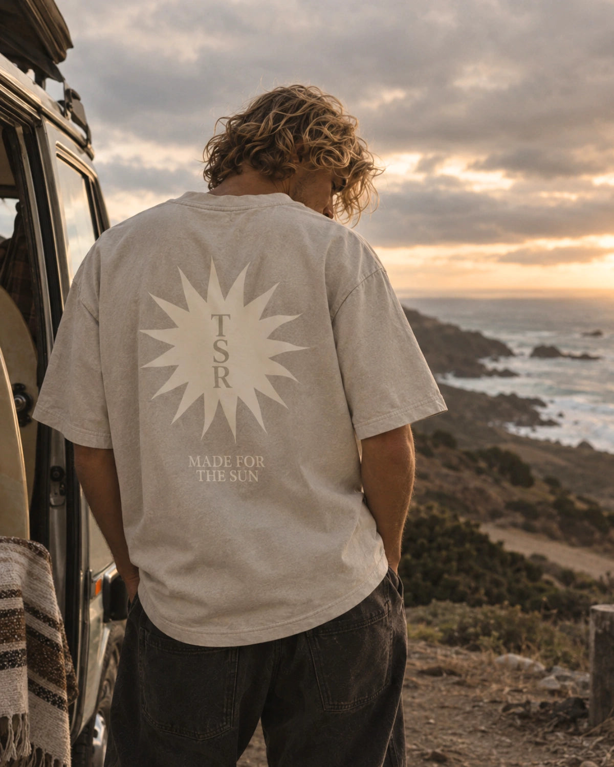 sunburst-boxy-tee-stone-frontprint-detail.webp

6. Herren Lifestyle – Camper, Rückseite

Alt-Text: Mann trägt das Sunburst Boxy Tee in Stone mit großem „Made for the Sun“-Backprint an einem Camper bei Sonnenuntergang.