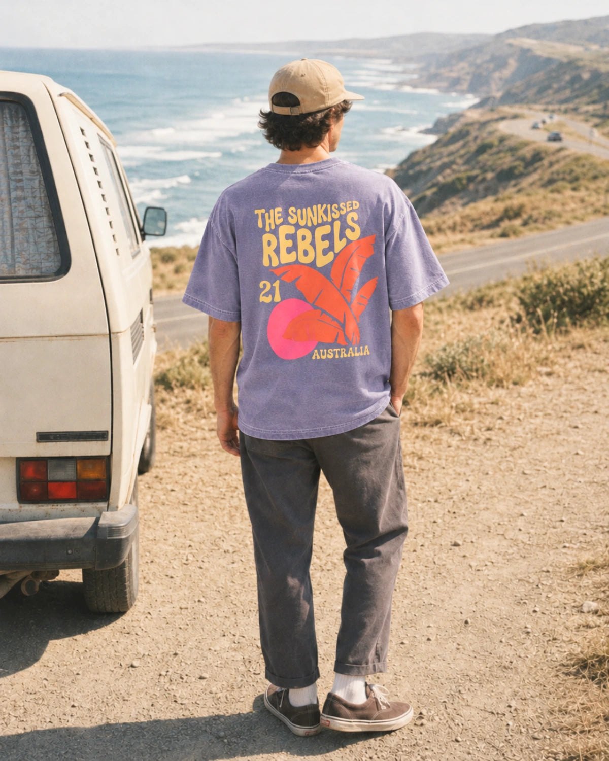 Mann trägt das Sunkissed Rebels Heavy Tee in Vintage Violet mit Oversized Fit und dezentem Backprint an einem Camper an der Küste.