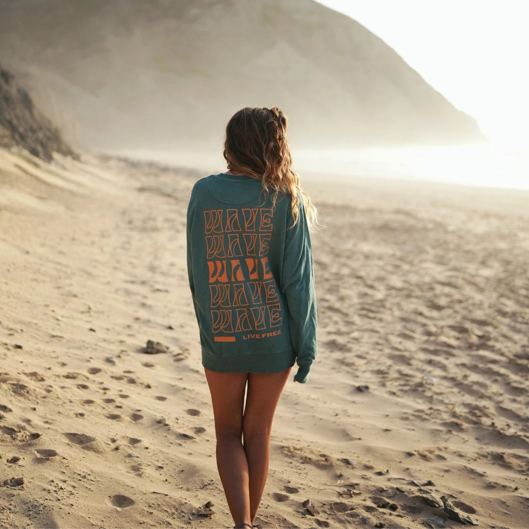 Frau am Strand mit grünem 'WAVE LIVE FREE' Longsleeve