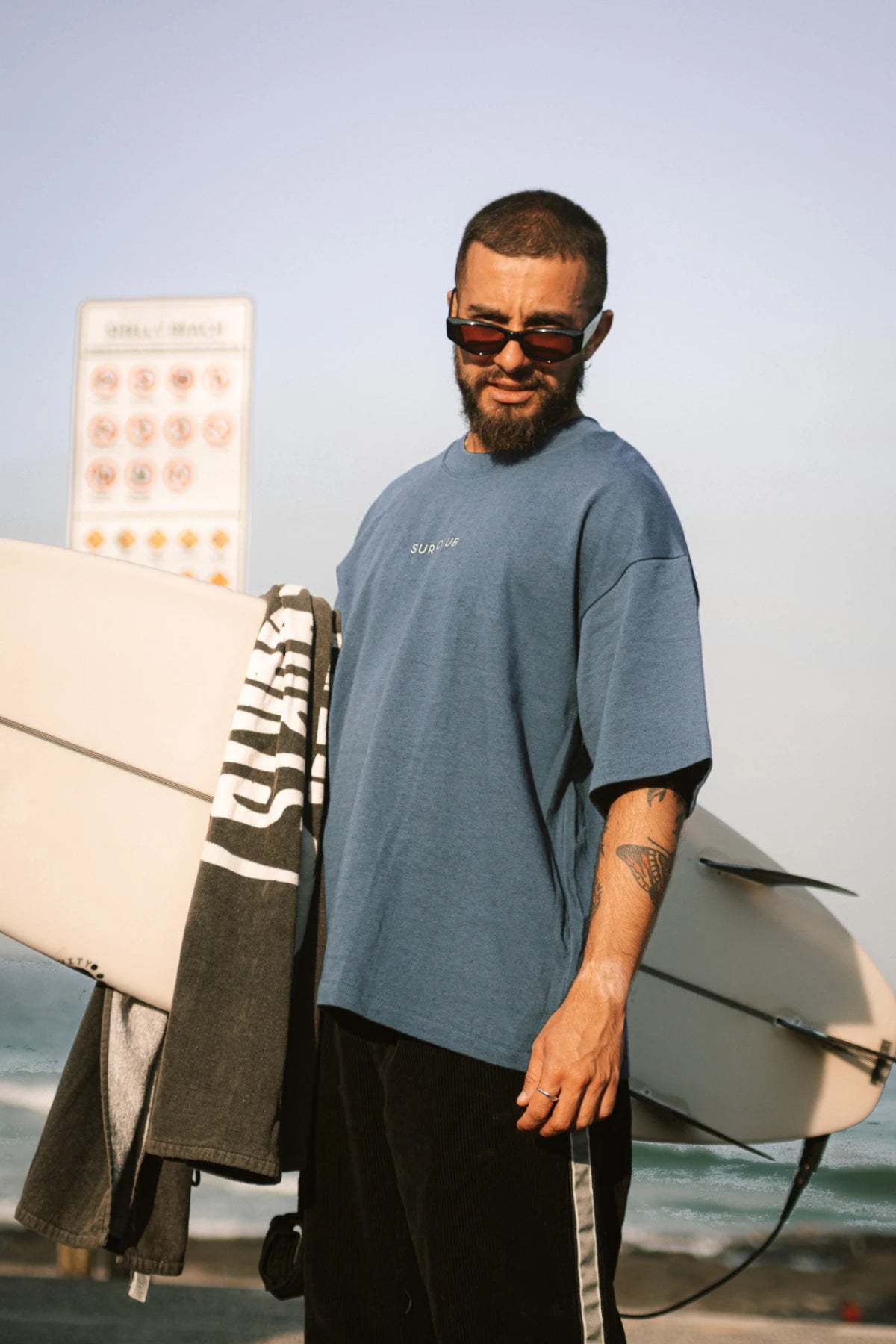 Surf Club Heavy T-Shirt – Deep Blue von The Sunkissed Rebels im goldenen Abendlicht, Surfmode für Herren mit entspannter Passform.