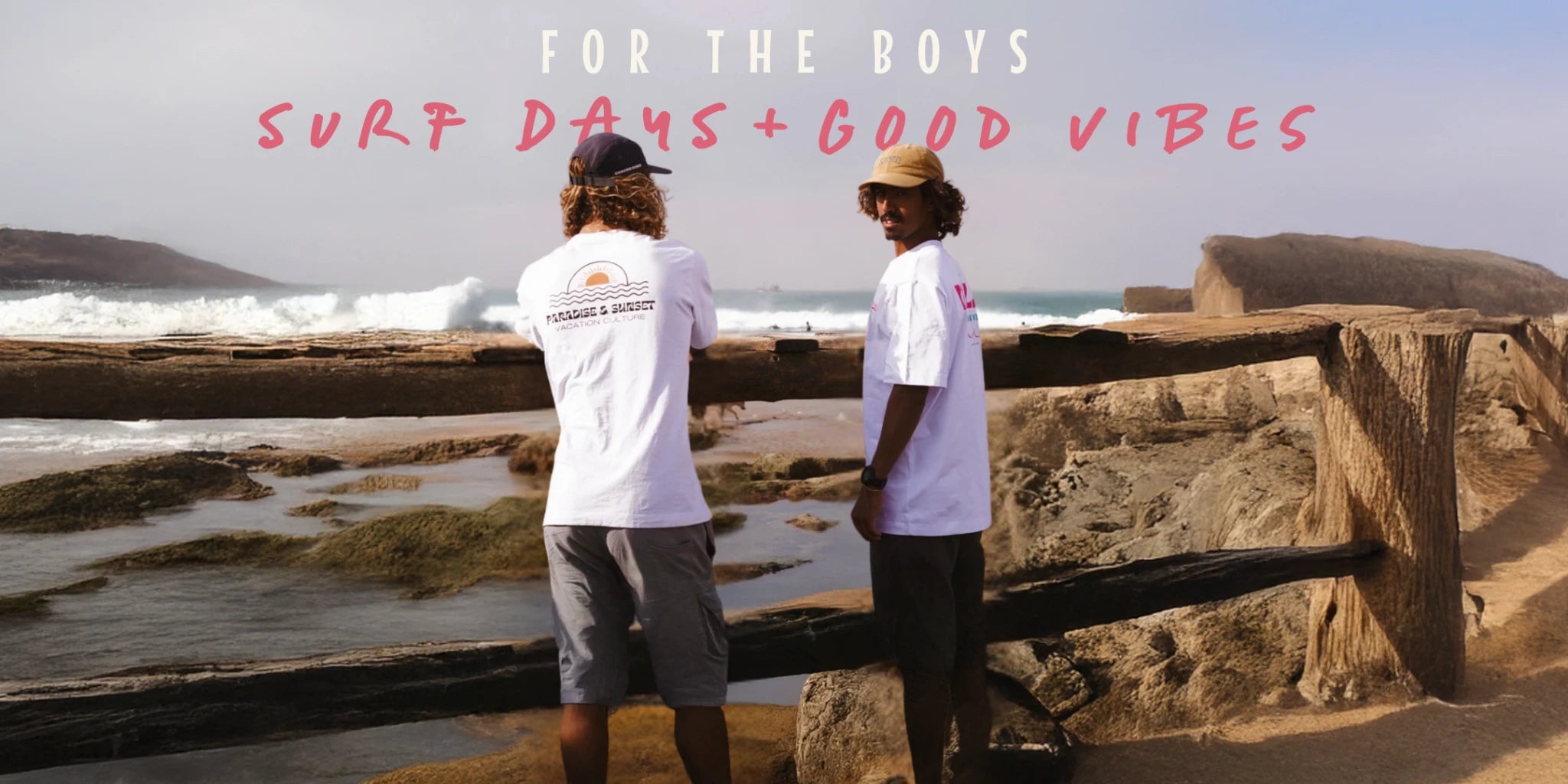 Zwei Männer in weißen 'Paradise & Sunset' T-Shirts stehen am Strand mit Blick auf das Meer – Surf-Style trifft Sommermode