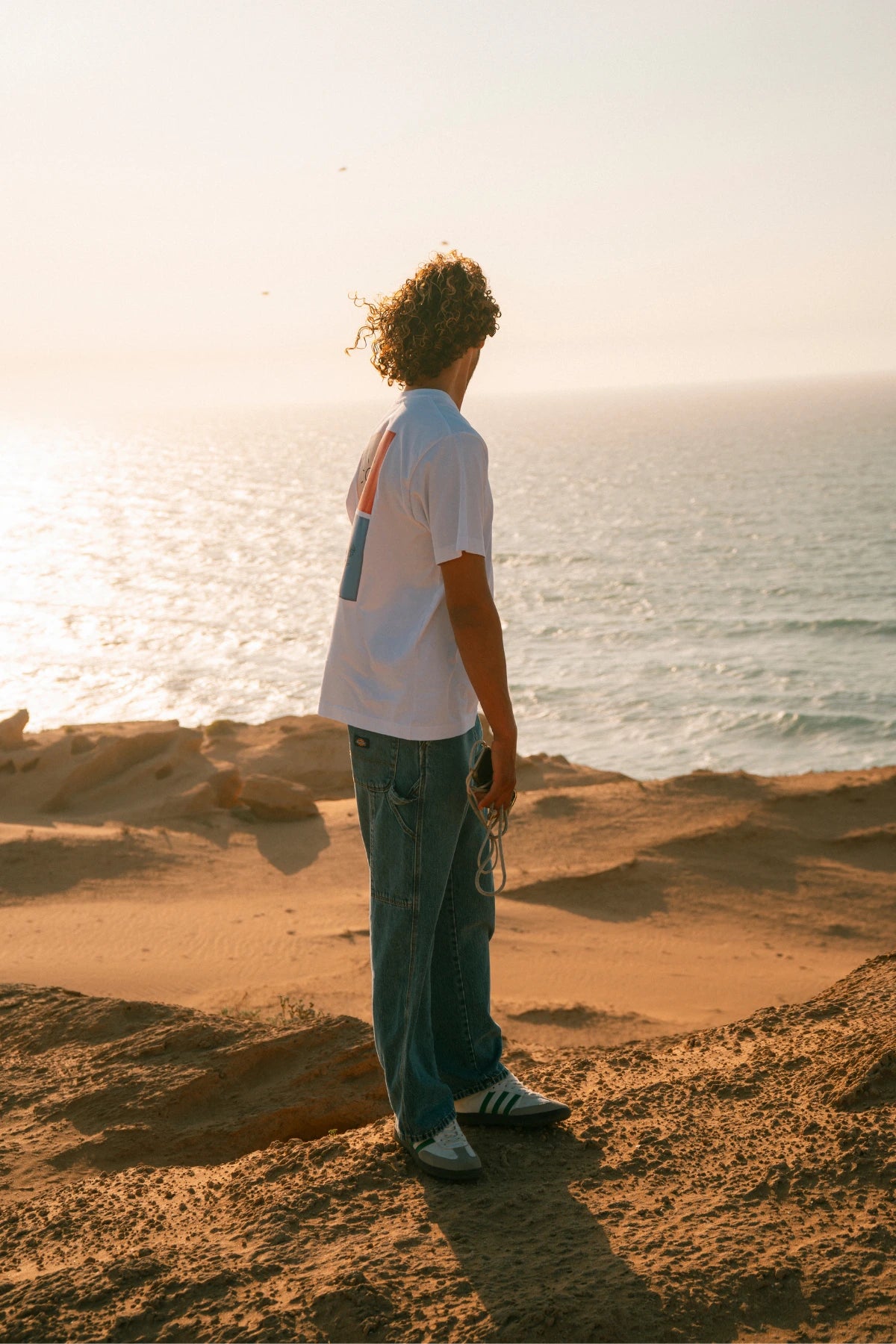 The Rebel Elements T-Shirt White Seitenansicht Backprint getragen am Meer minimalistisches Design