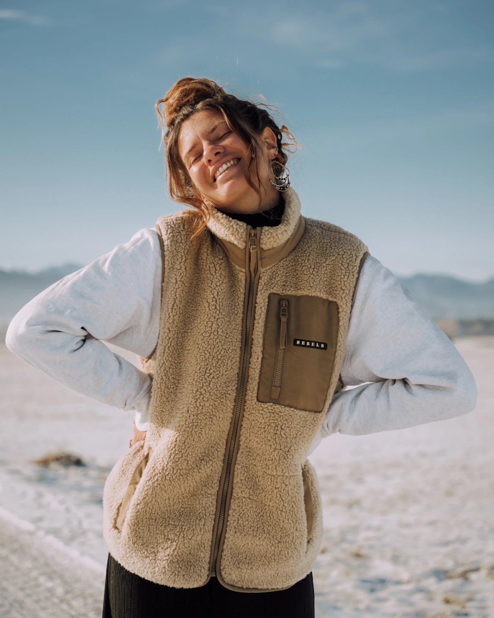 Frau trägt beige Fleece Weste von The Sunkissed Rebels am Strand mit geschlossenen Augen im Sonnenlicht