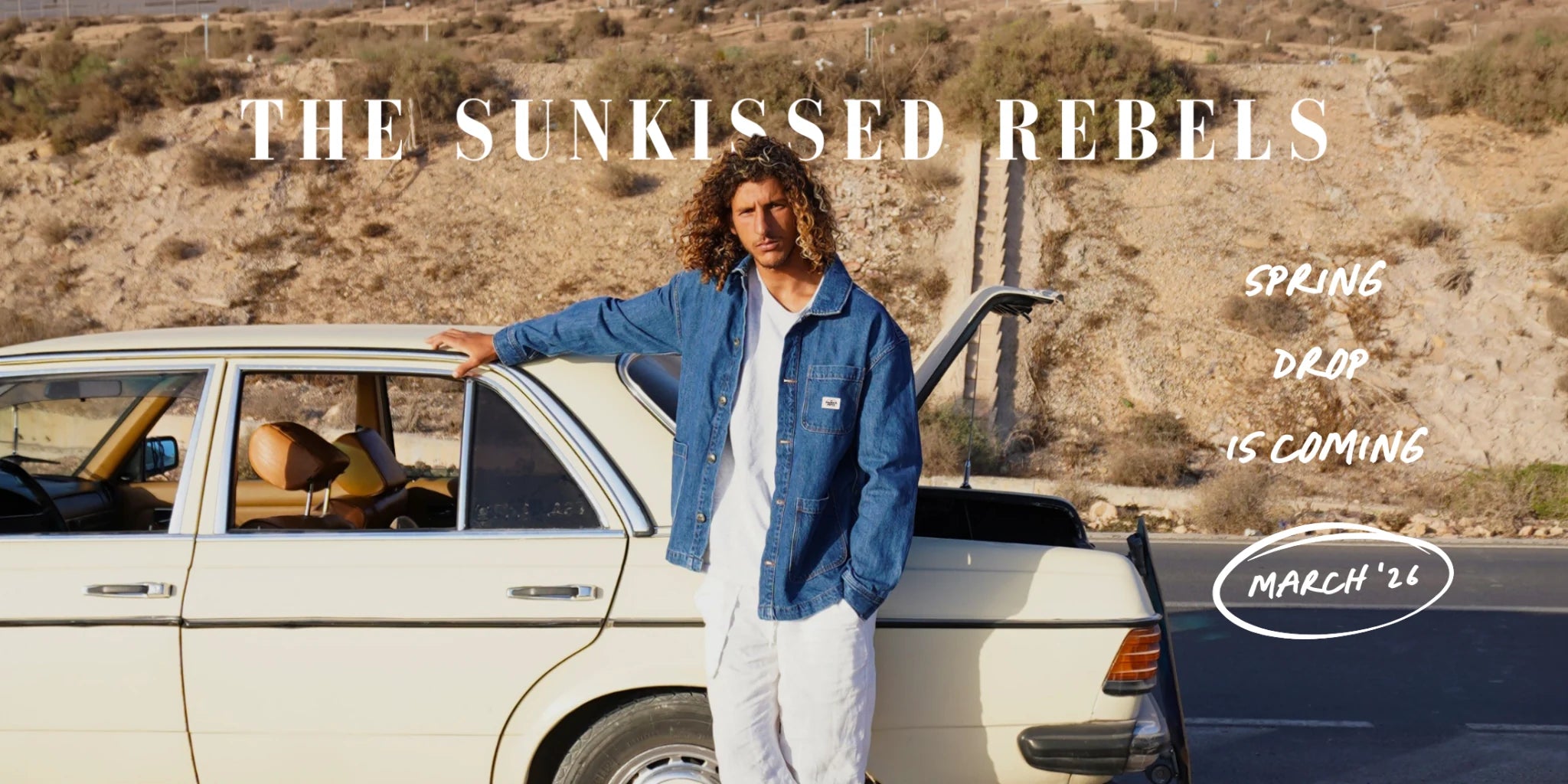 The Sunkissed Rebels Spring Drop 2026 – Model im nachhaltigen Vintage Denim Jacket neben klassischem Oldtimer in sonniger Wüstenkampagn