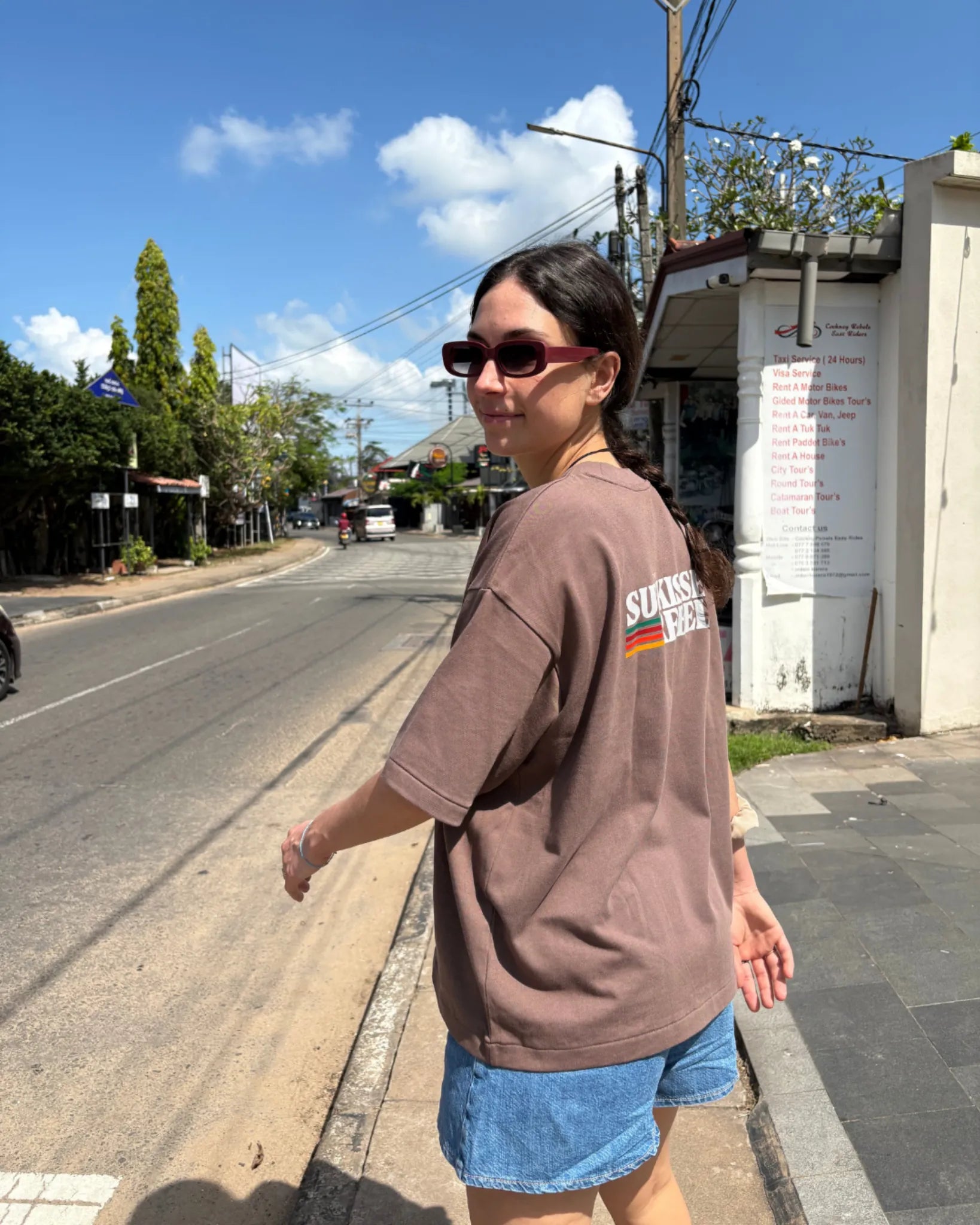 Frau trägt braunes Logo T-Shirt von The Sunkissed Rebels in urbaner Sommerkulisse