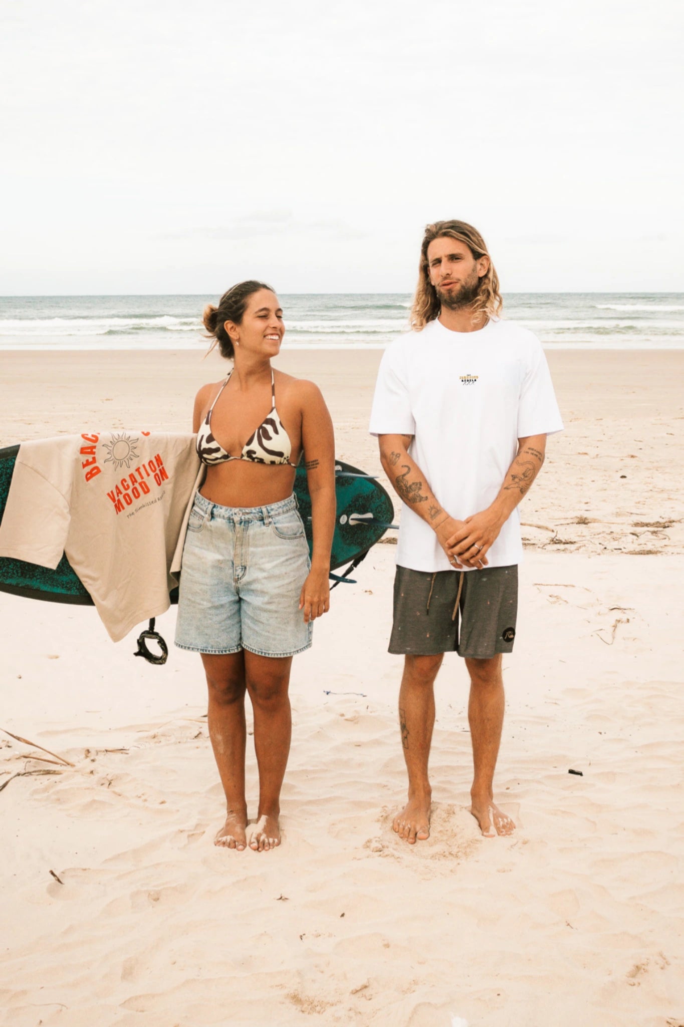 Weißes T-Shirt „Paradise & Sunsets“ von The Sunkissed Rebels am Strand getragen – nachhaltige Surf & Beach Streetwear.