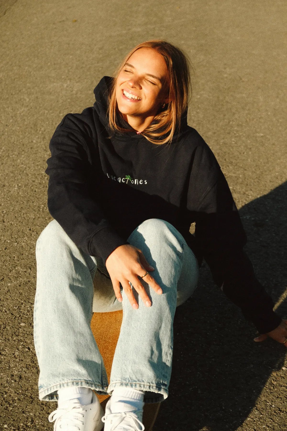 Frau sitzt lachend in der Sonne und trägt den Vacaciones Oversized Hoodie Dark Oce