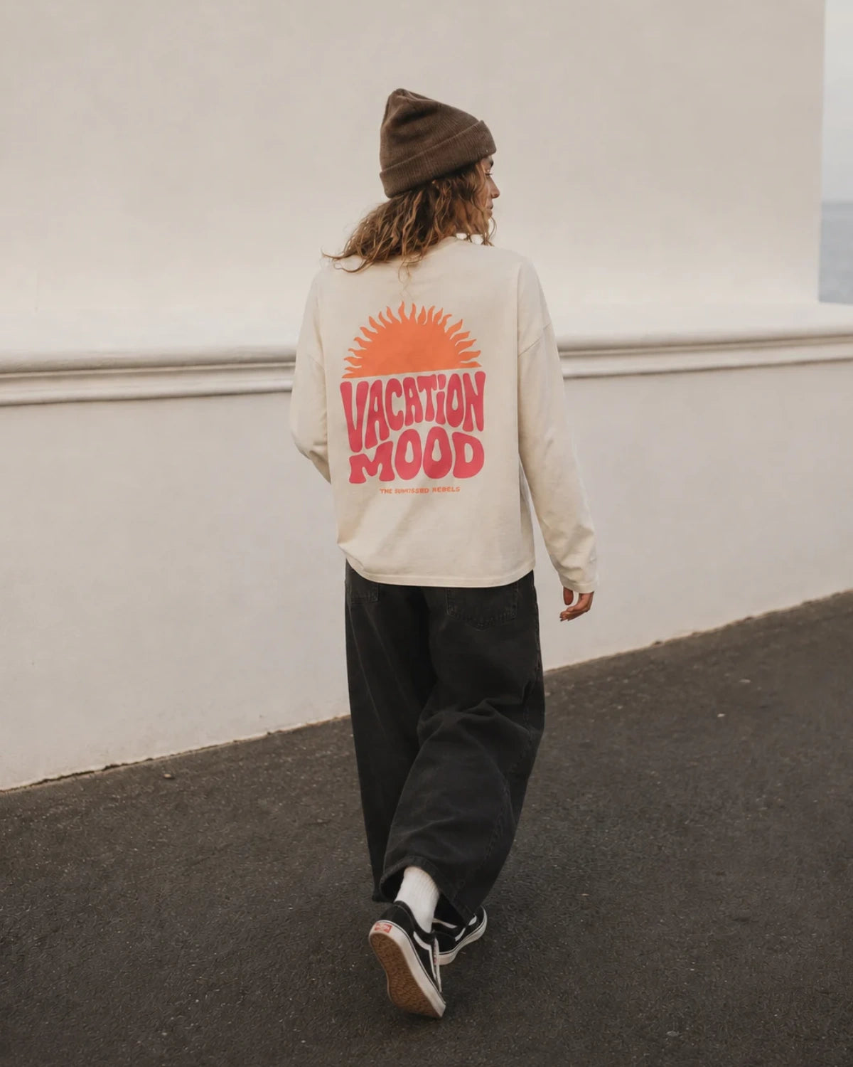 Nahaufnahme einer Frau im Vacation Mood Longsleeve in Natural Raw mit korallfarbenem TSR-Sonnenlogo auf der Brust.