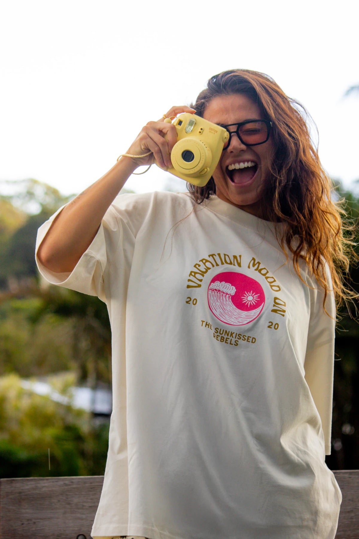 Lachende Frau mit Kamera im Vacation Mood On T-Shirt von The Sunkissed Rebels – Cream