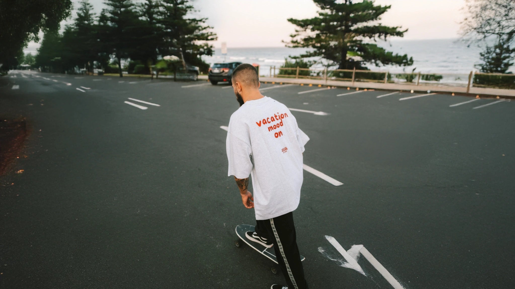 Mann mit Skateboard trägt graues Oversized T-Shirt mit rotem Druck